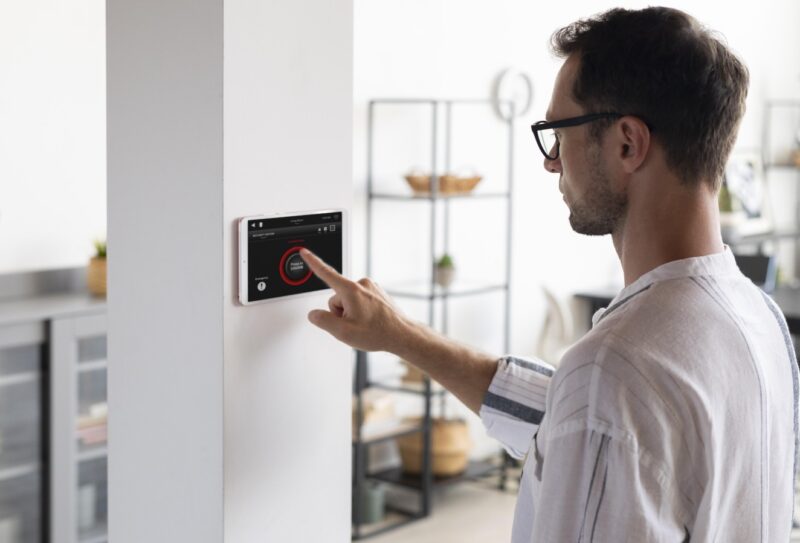 Man wearing glasses using a wall-mounted touchscreen to control a home security alarm system